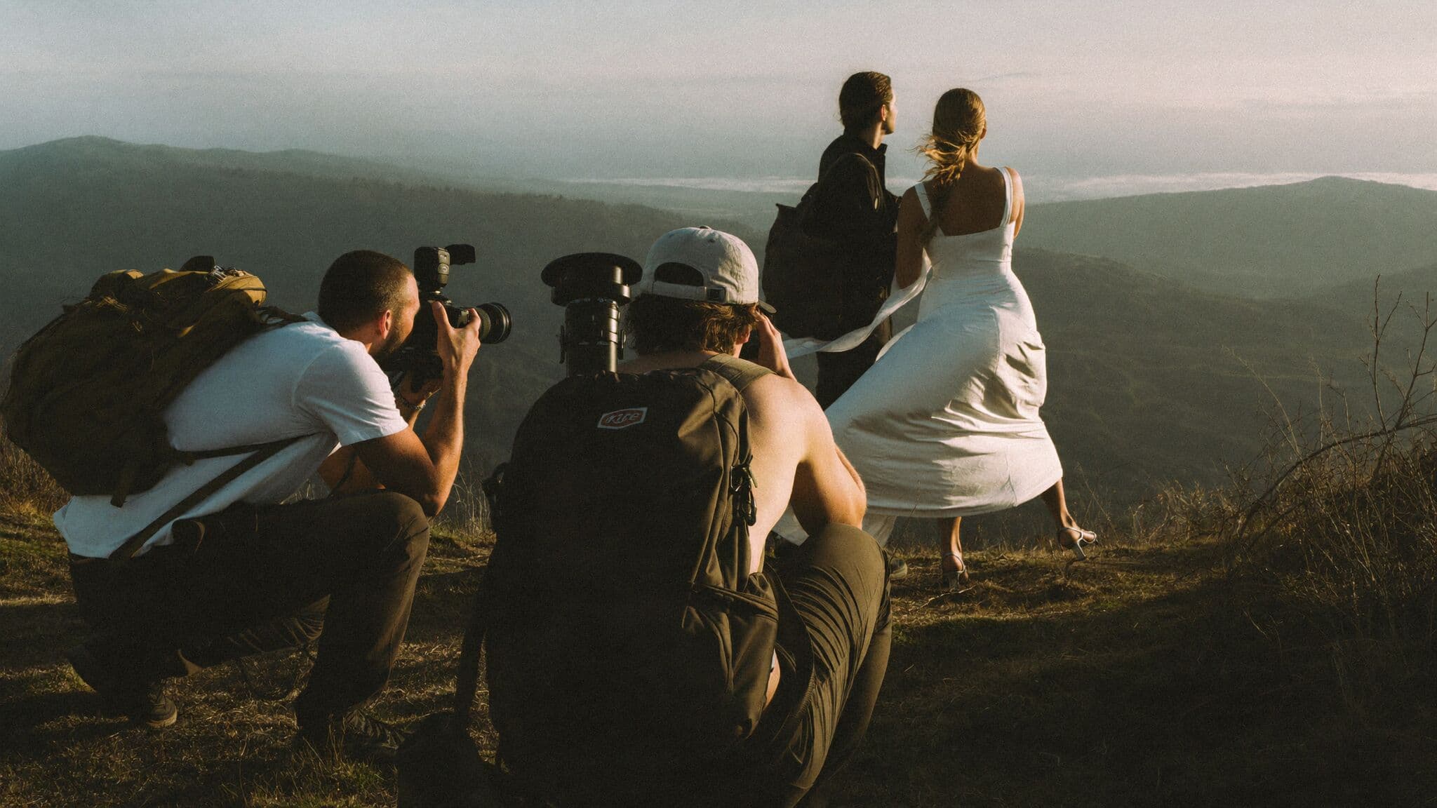Two adventure elopement photographers photographing a couple on a mountain ridge at golden hour