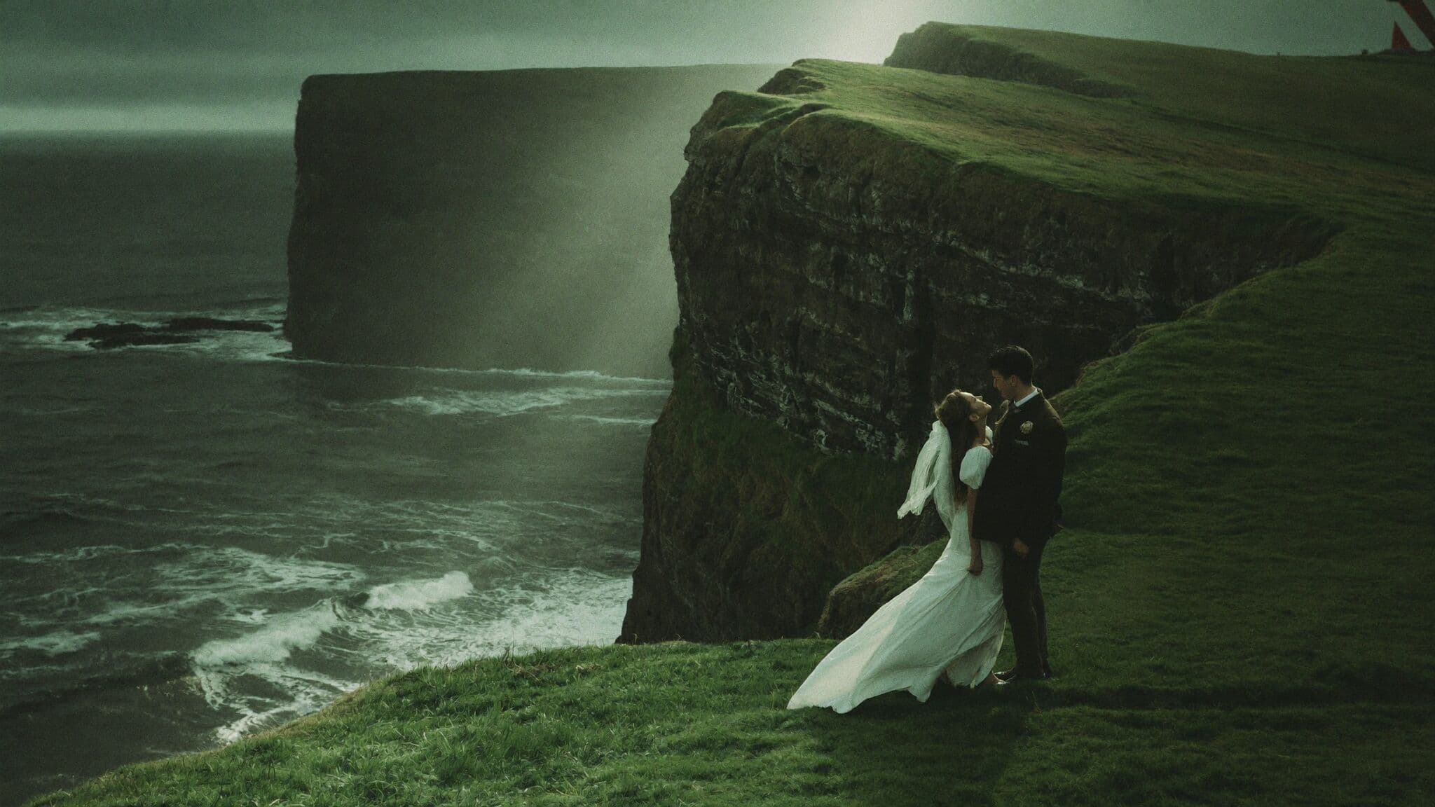 Couple standing near Kallur lighthouse on Kalsoy's grassy ridgeline during their Faroe Islands elopement