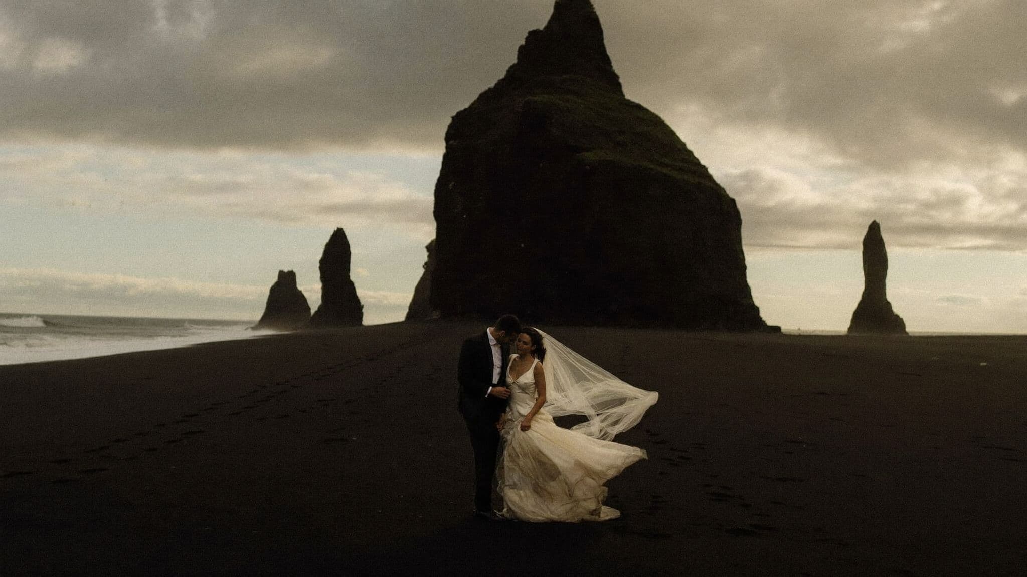 Couple embracing on Reynisfjara black sand beach with basalt sea stacks, Iceland elopement