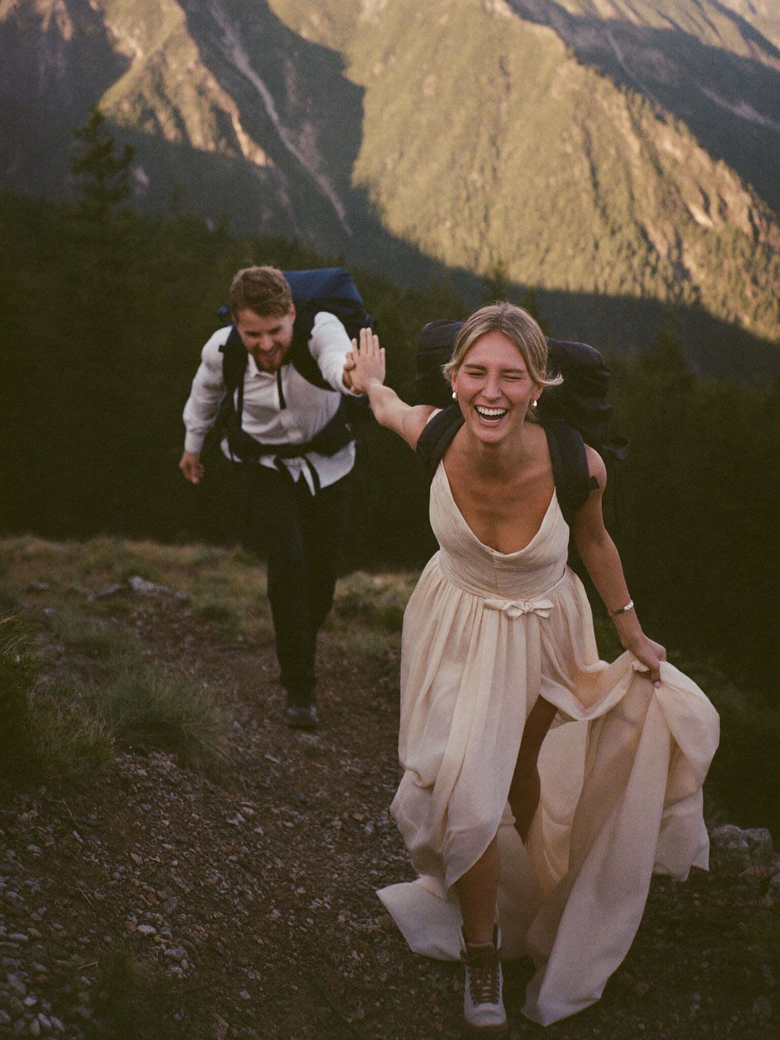 Bride in hiking boots and wedding dress climbing a mountain trail with her groom during their elopement