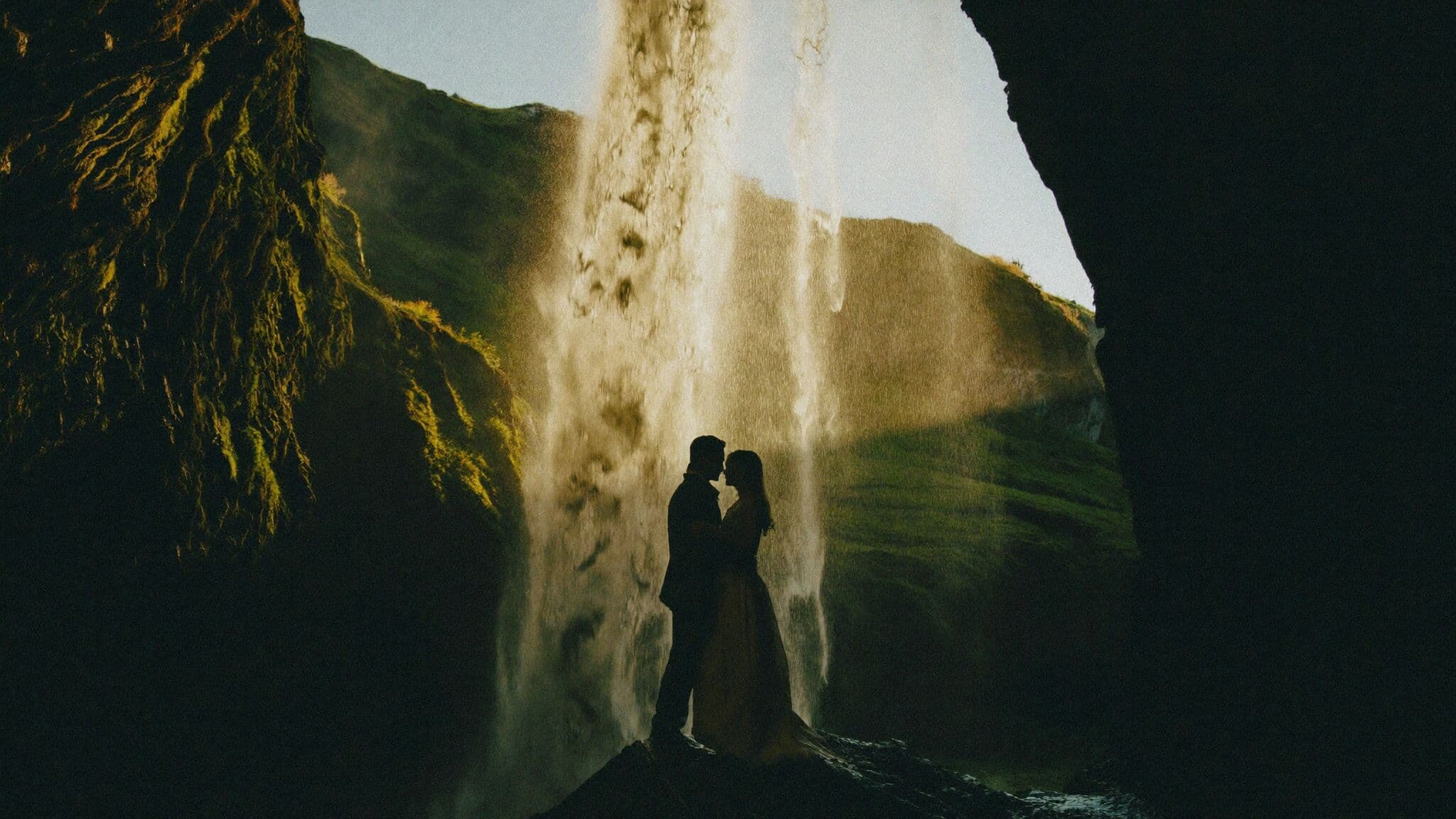 Couple kissing behind Seljalandsfoss waterfall at golden hour during Iceland elopement