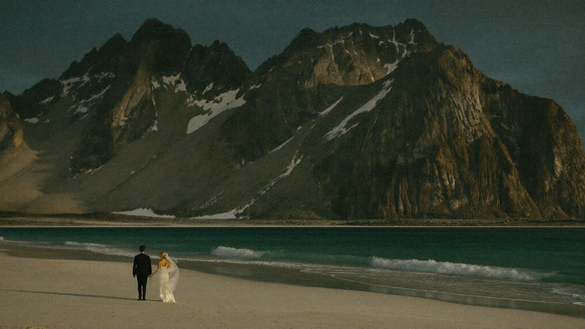 Couple walking the white sand of Haukland Beach beneath granite peaks during their Lofoten, Norway elopement