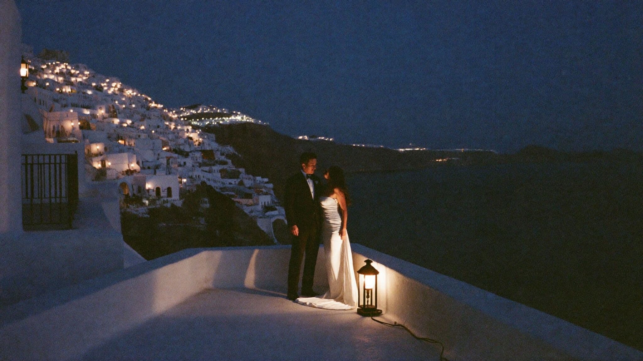 Couple on a caldera terrace at blue hour with village lights glowing, Santorini elopement