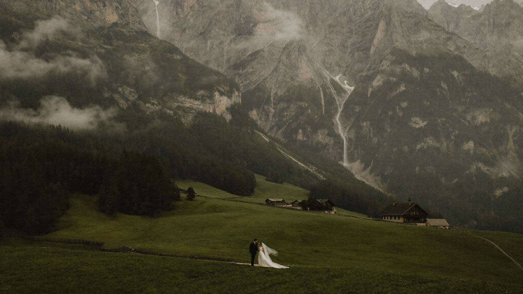 Couple in wedding attire on a meadow above Lauterbrunnen valley with Staubbach Falls behind them during their Switzerland elopement