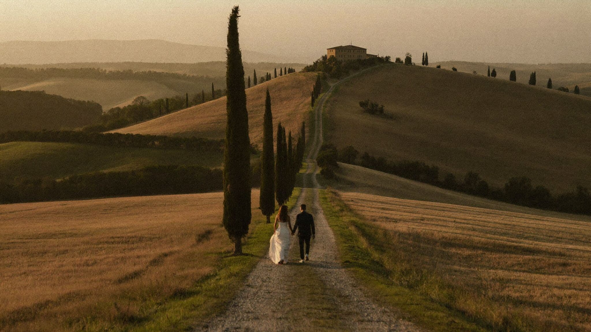 Couple walking a cypress-lined gravel road in the Val d'Orcia during their Tuscany elopement