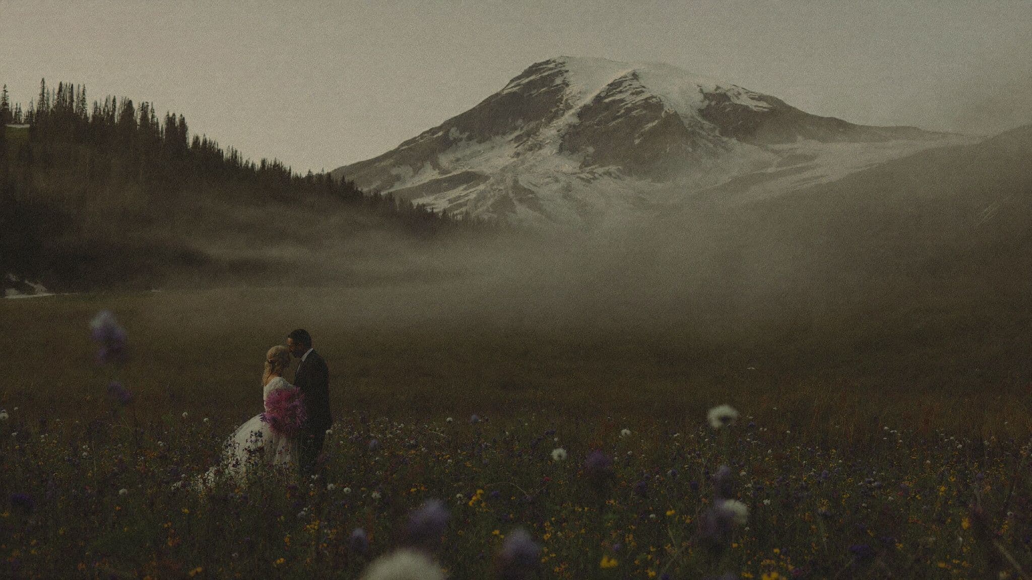 Couple standing in a wildflower meadow below Mount Rainier during their Washington elopement